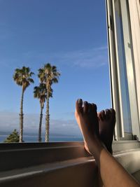 Low section of woman with feet on window sill against blue sky