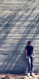 Rear view of man standing on footpath against wall