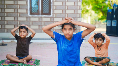 Three indian little kids doing meditate yoga asana on roll mat at home.