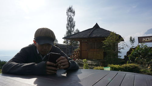Man using mobile phone on table outdoors against sky