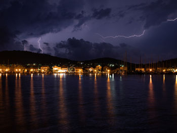 Illuminated city by sea against sky at night