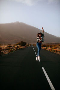 Full length of happy woman walking on road against sky