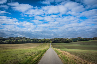 Empty road amidst field against sky