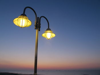 Low angle view of illuminated lamp by sea against sky
