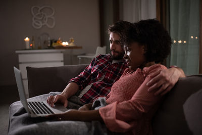 Multiethnic couple watching movie on sofa together