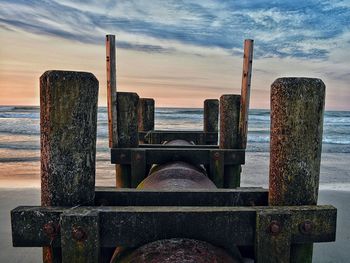 Abandoned pier at beach against sky