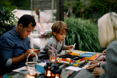 Family playing board game on table while father using mobile phone