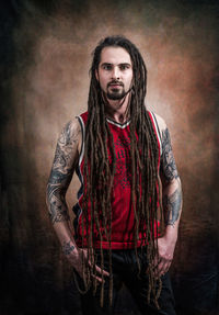 Portrait of young man with dreadlocks standing against wall