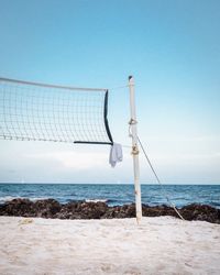 Net at beach against sky during sunny day