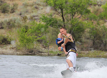 Full length of man wake boarding with child 