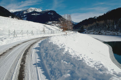 Snow covered road by mountains against sky