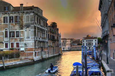 Canal amidst buildings in city against sky during sunset