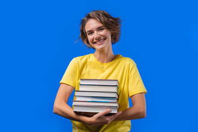 Portrait of young woman sitting against blue background