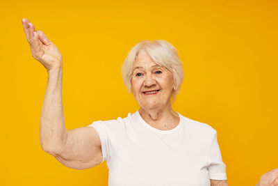 Senior woman gesturing against yellow background