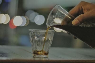 Cropped hand holding pouring drink in glass on table
