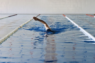 Anonymous male swimming in crawl style in pool during training