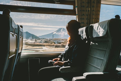 Side view of woman sitting in bus against sky