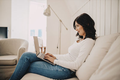 Young woman using mobile phone while sitting on sofa at home