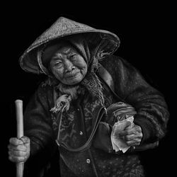 Portrait of senior woman wearing asian style conical hat against black background