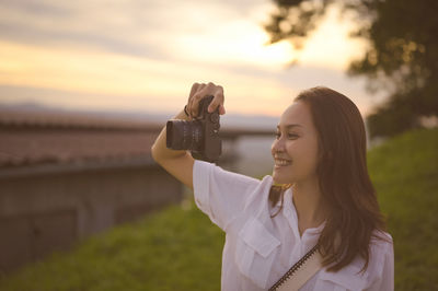 Young woman photographing while standing outdoors