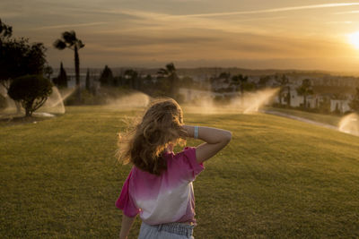 Rear view of woman standing on field against sky during sunset