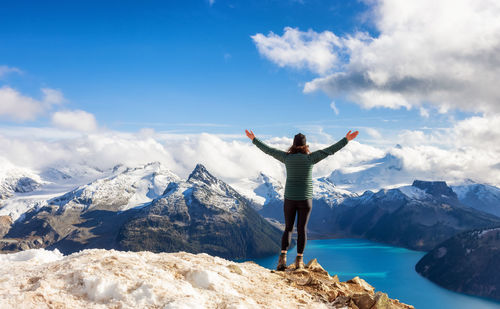 Rear view of person standing on snowcapped mountain against sky