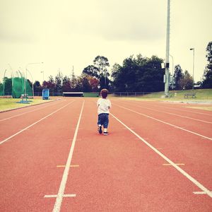 Rear view of boy on running track against sky