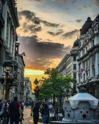 People on street amidst buildings in city during sunset