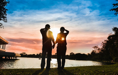 Rear view of silhouette couple standing by lake against sky during sunset