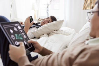 Brothers lying on bed and using phone and tablet