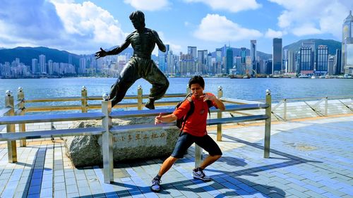 Full length of man gesturing against statue in city during sunny day