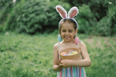 Girl with eggs basket and bunny ears on easter egg hunt in garden.