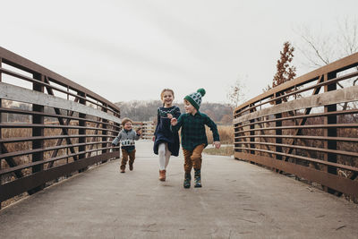 Siblings running together on bridge toward camera