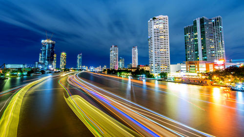 Light trails on city buildings against sky at night