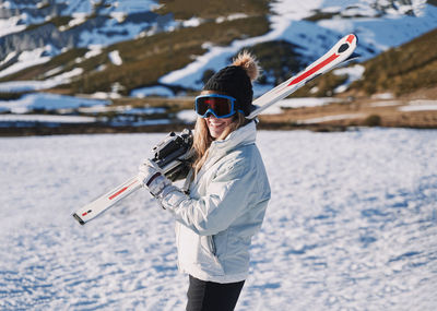 Woman wearing ski goggles while standing on snow covered land