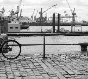 Bicycle parked on bridge against cranes at harbor