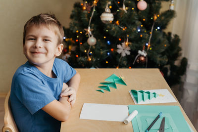 Smiling child making christmas card. glue the prepared parts of the christmas tree on the card sheet