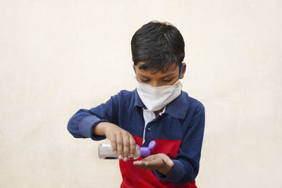 Close-up of boy wearing flu mask using hand sanitizer against wall