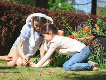 Two girls sisters with bunny ear rims collect scattered chocolate easter eggs in shiny wrappers 