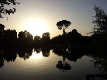 Silhouette trees by lake against sky during sunset