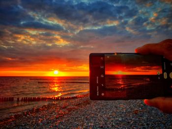 Person photographing sea against sky during sunset