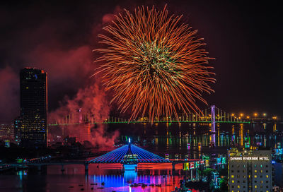 Firework display over illuminated buildings and river in city at night