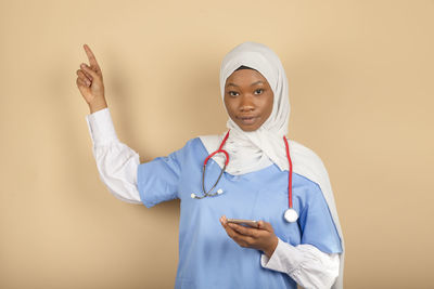 Muslim religion nurse online with headscarf isolated.holds smartphone, points finger up person