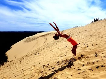 Side view of boy jumping on sand dune against sky