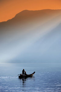 Silhouette man in sea against sky during sunset