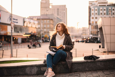 Young woman sitting on mobile phone in city