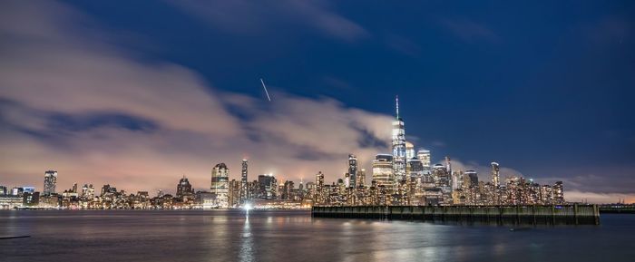 Illuminated buildings in city against cloudy sky