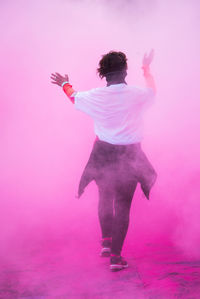 Rear view of woman dancing amidst pink powder paint