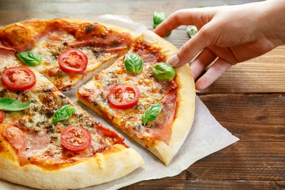 Cropped image of hand holding fresh margherita pizza with salami on wooden table