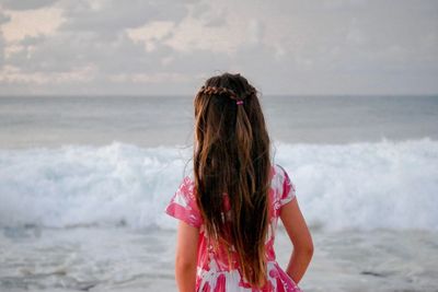 Rear view of woman standing on beach against sky